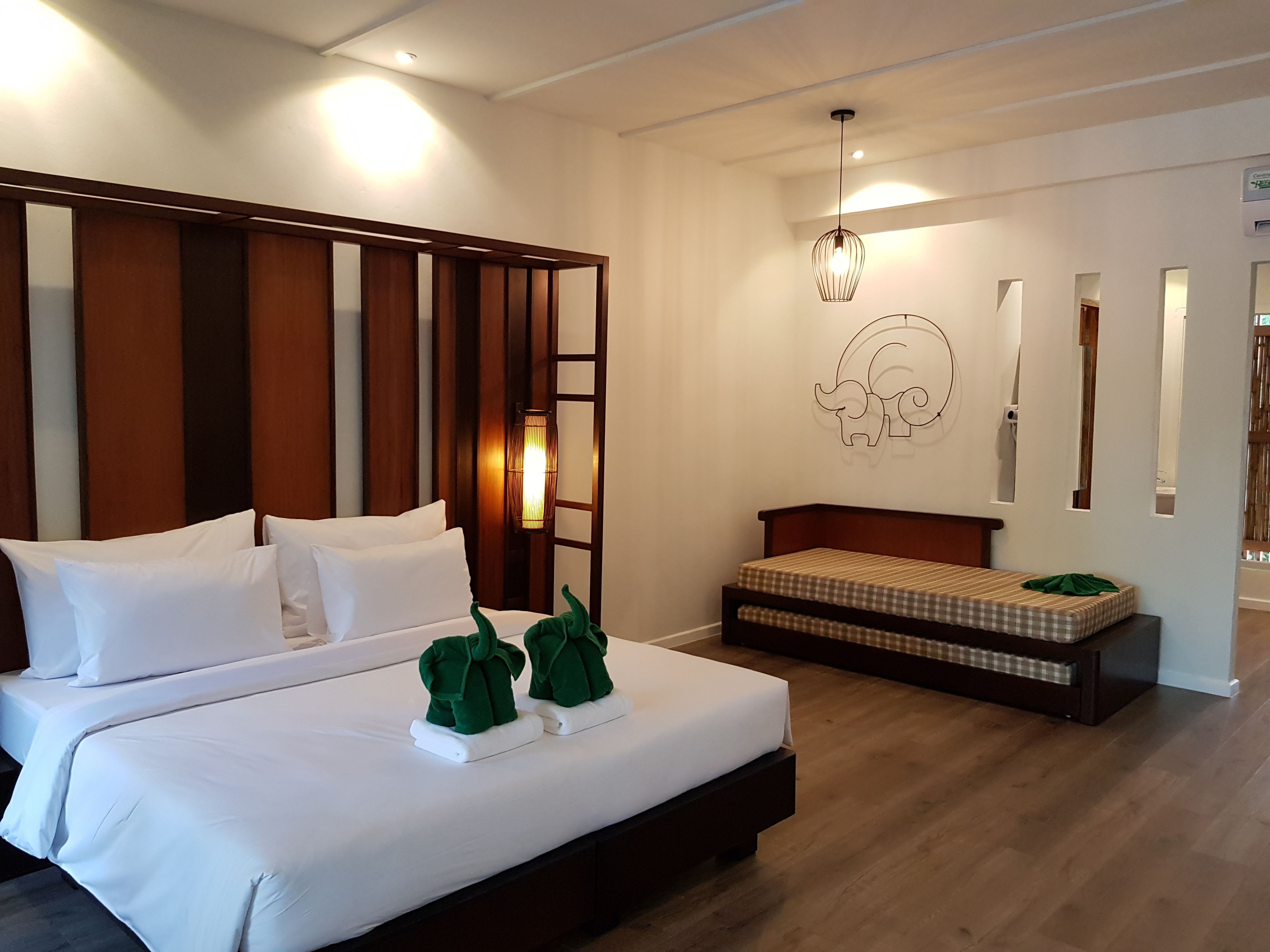 A hotel room with a large bed, a smaller bed, a wall-mounted elephant decoration, and a hanging light fixture.