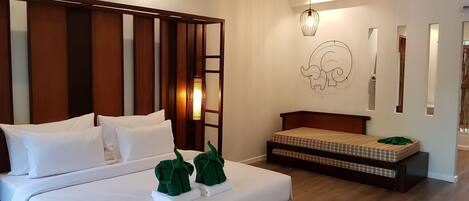A hotel room with a large bed, a smaller bed, a wall-mounted elephant decoration, and a hanging light fixture.