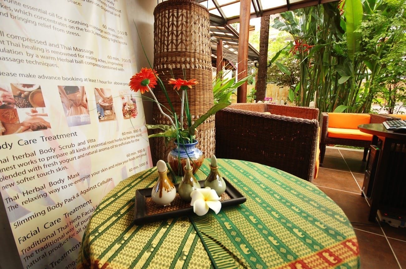 A brochure for Thai massage services, a wicker chair, a table with a green mat, and a vase with flowers.