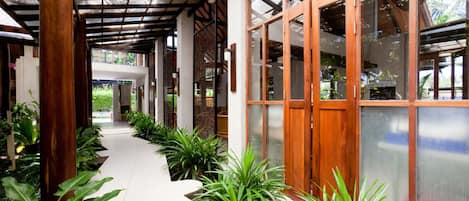 A covered walkway with wooden pillars, glass doors, and potted plants.