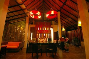 A reception area with a wooden ceiling, two red hanging lights, a reception desk, and a seating area with orange cushions.