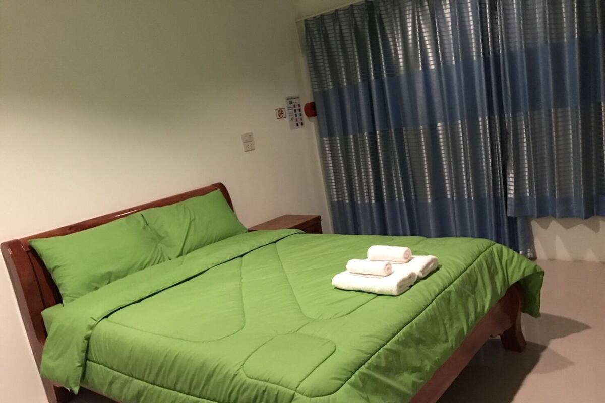 A neatly made bed with green bedding and two rolled towels on the footboard.