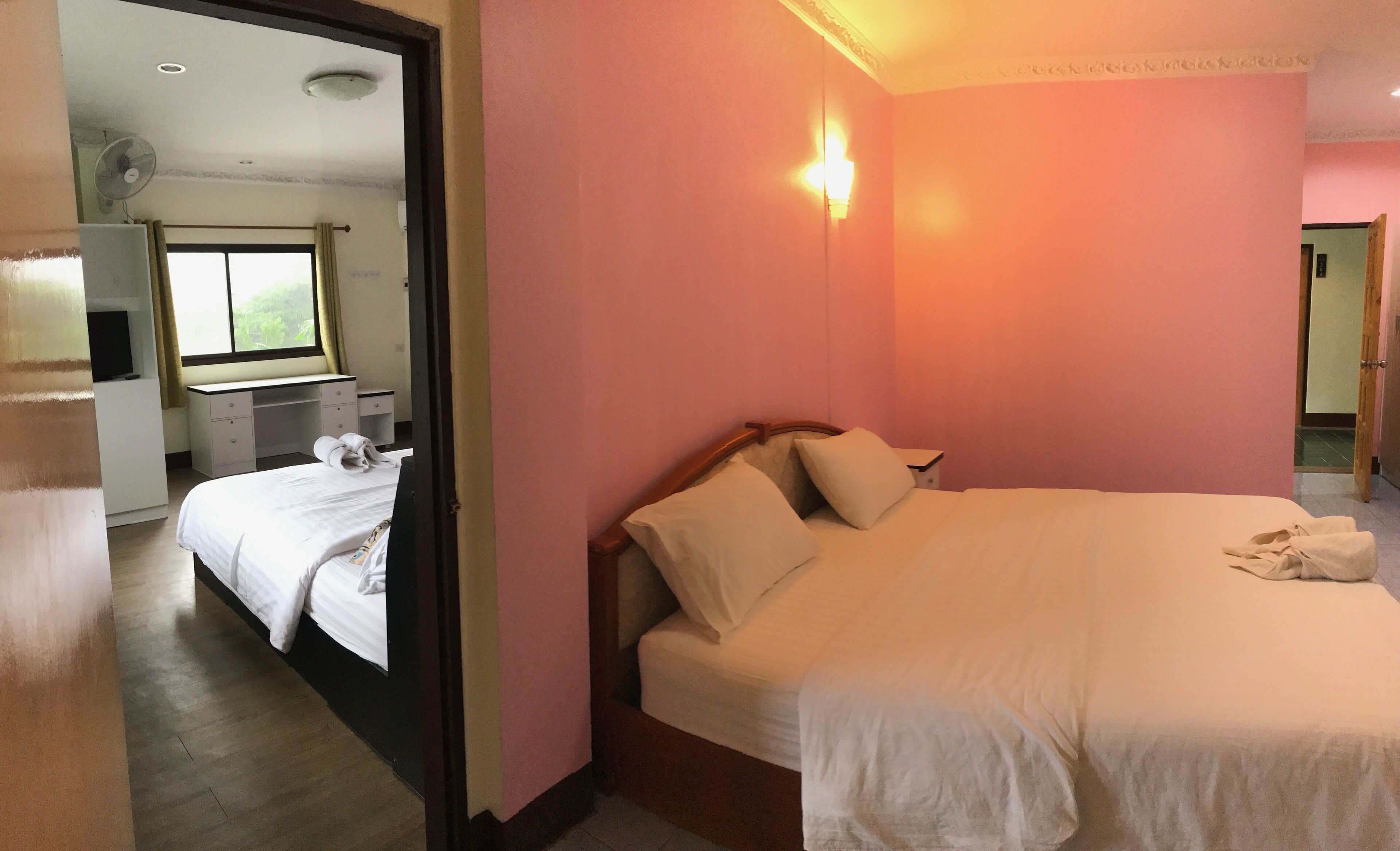 A hotel room with a large bed, a desk with a chair, a window with curtains, and a wall-mounted light.