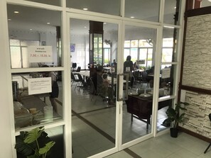 A restaurant with a breakfast time sign, tables, chairs, and a stone wall. - The Great Rayong Hotel (Rayong)
