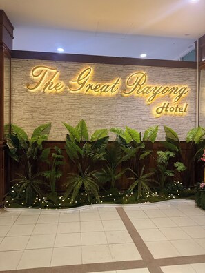 A hotel entrance with a neon sign reading 'The Great Rajong Hotel' above a wall of greenery. - The Great Rayong Hotel (Rayong)