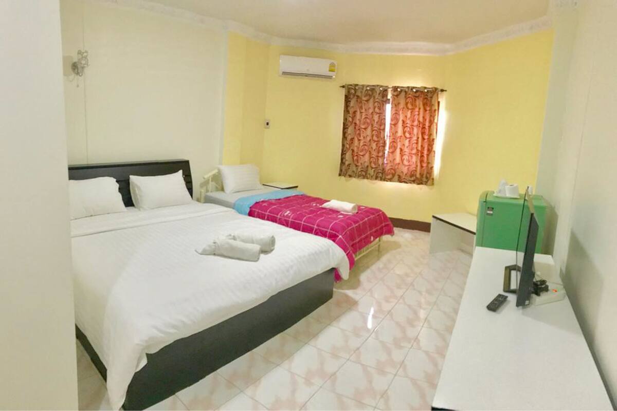 A hotel room with two beds, a desk, a chair, an air conditioning unit, and a window with curtains.