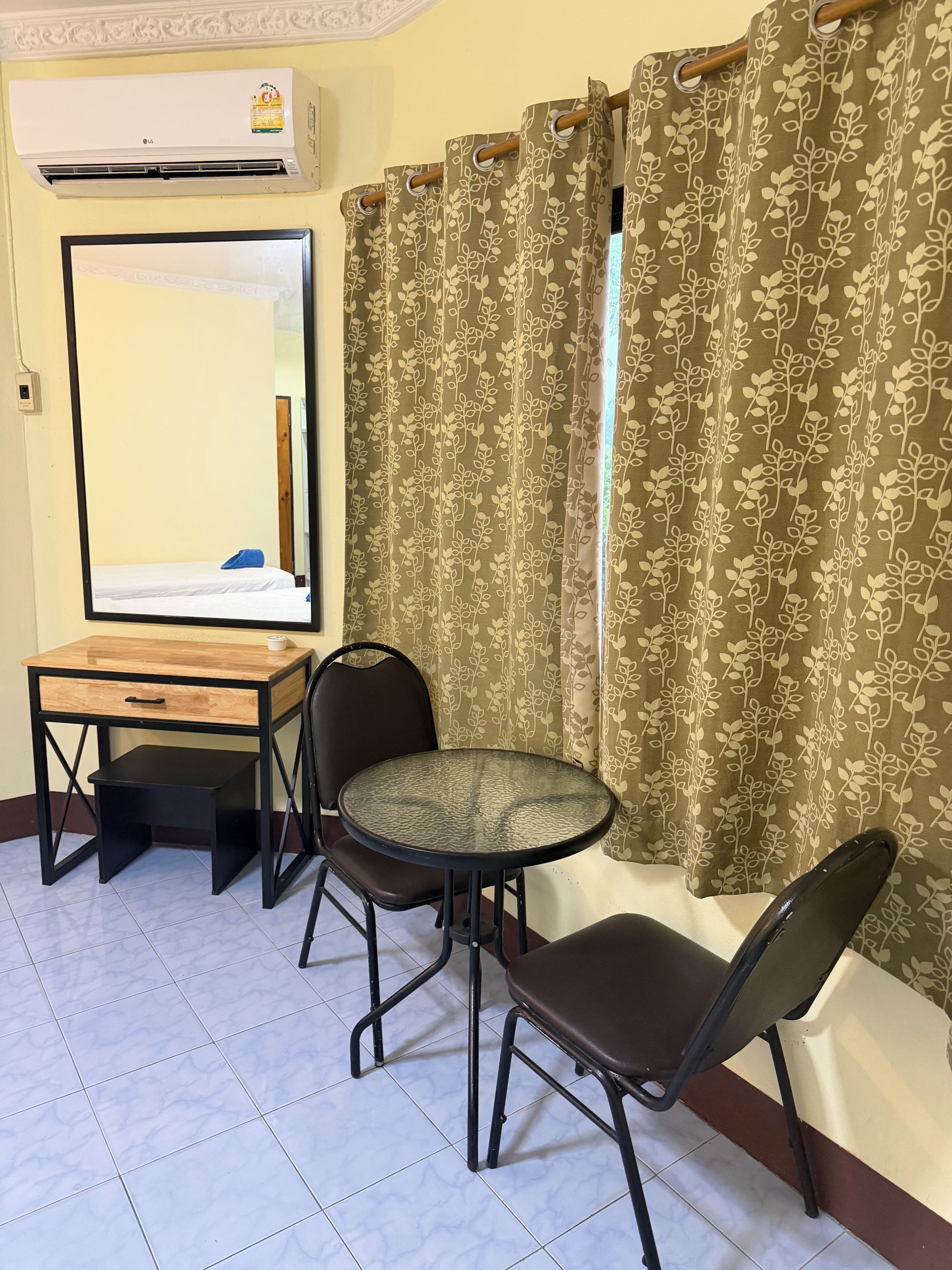 A room with a bed, a mirror, a small table with a chair, and a window with curtains.