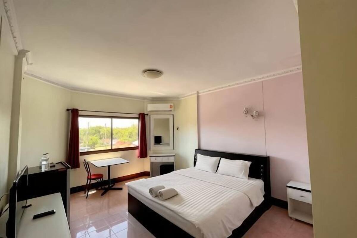 A hotel room with a bed, a desk, a chair, a small table, a mirror, and a window.