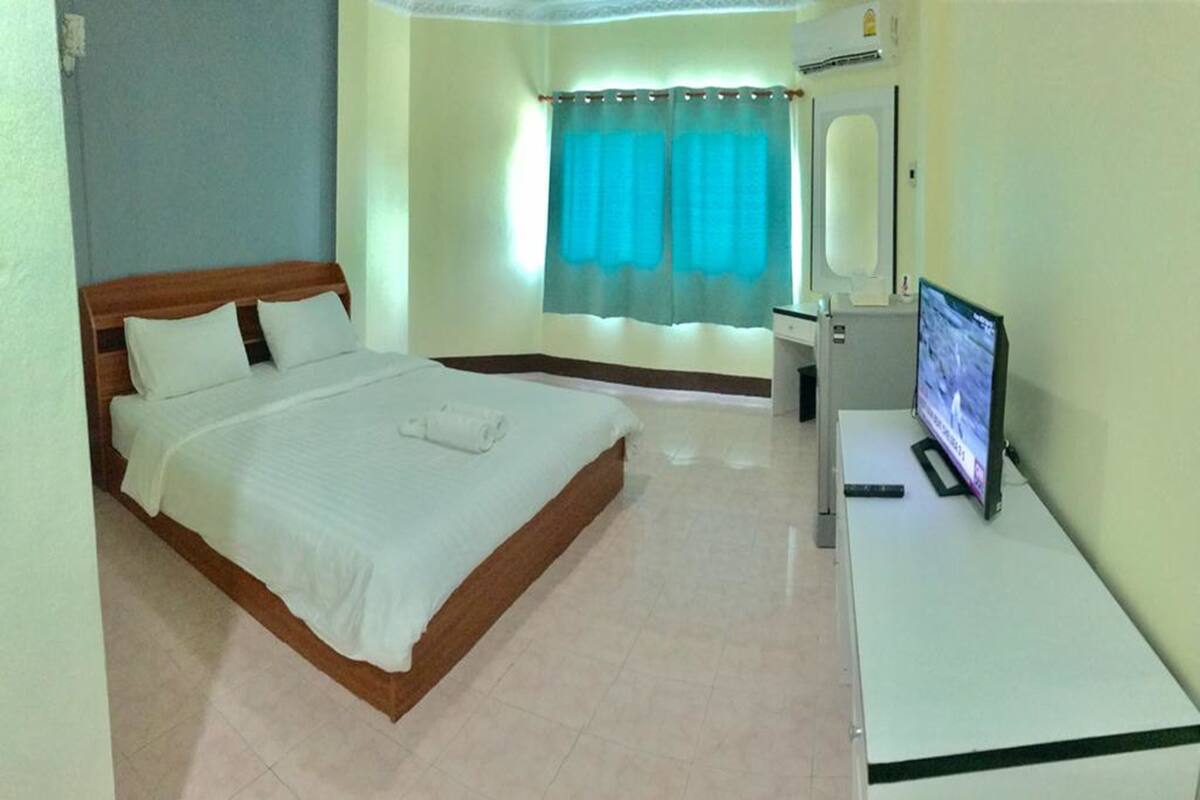 A hotel room with a bed, a desk with a computer, and a window with curtains.