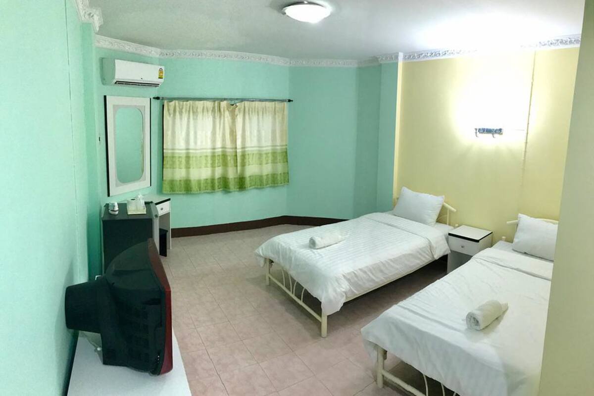 A room with two beds, a desk, a chair, an air conditioner, and a window with curtains.