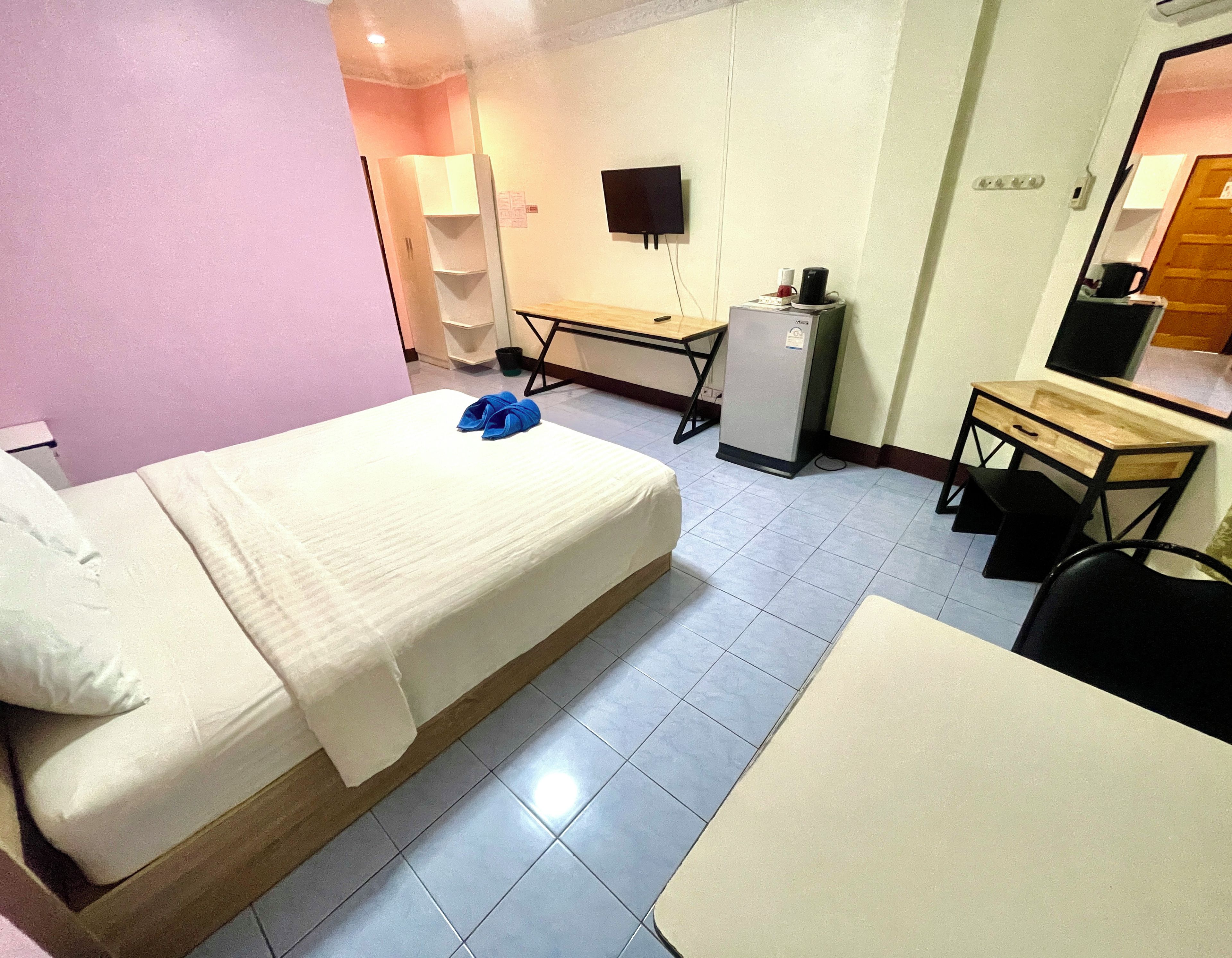 A hotel room with a bed, a desk, a chair, a small refrigerator, and a television.