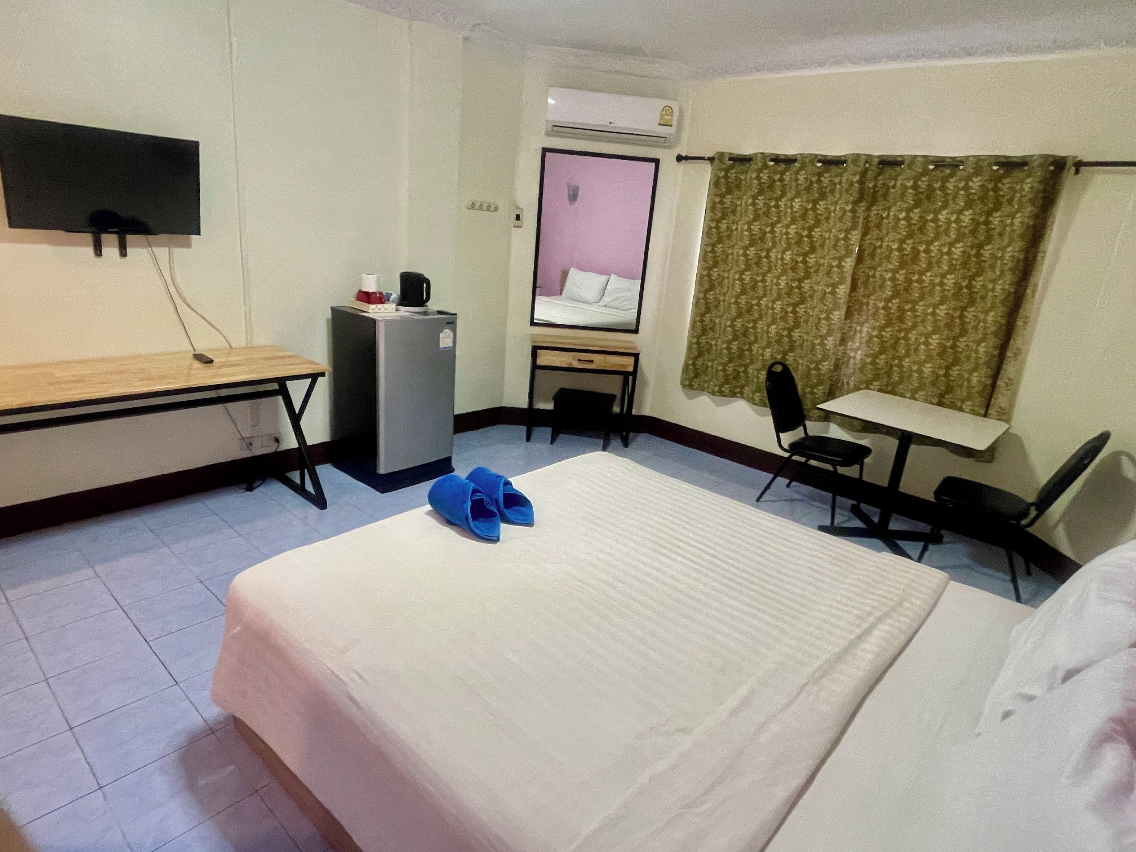 Ein Hotelzimmer mit Bett, Schreibtisch, Sessel, kleinem Kühlschrank und Wandfernseher.
