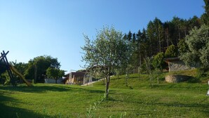 Une zone herbeuse avec une aire de jeux, un bâtiment en pierre et, au loin, une colline boisée.