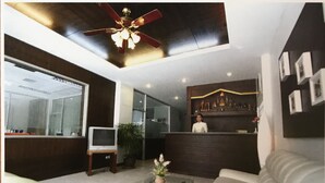A modern living room with a ceiling fan, a TV, a sofa, a coffee table, and a bar area with a person behind the counter. - PK Mansion (Wichit)