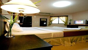 A hotel room with a bed, a desk, a lamp, a television, and a window with curtains. - PK Mansion (Wichit)