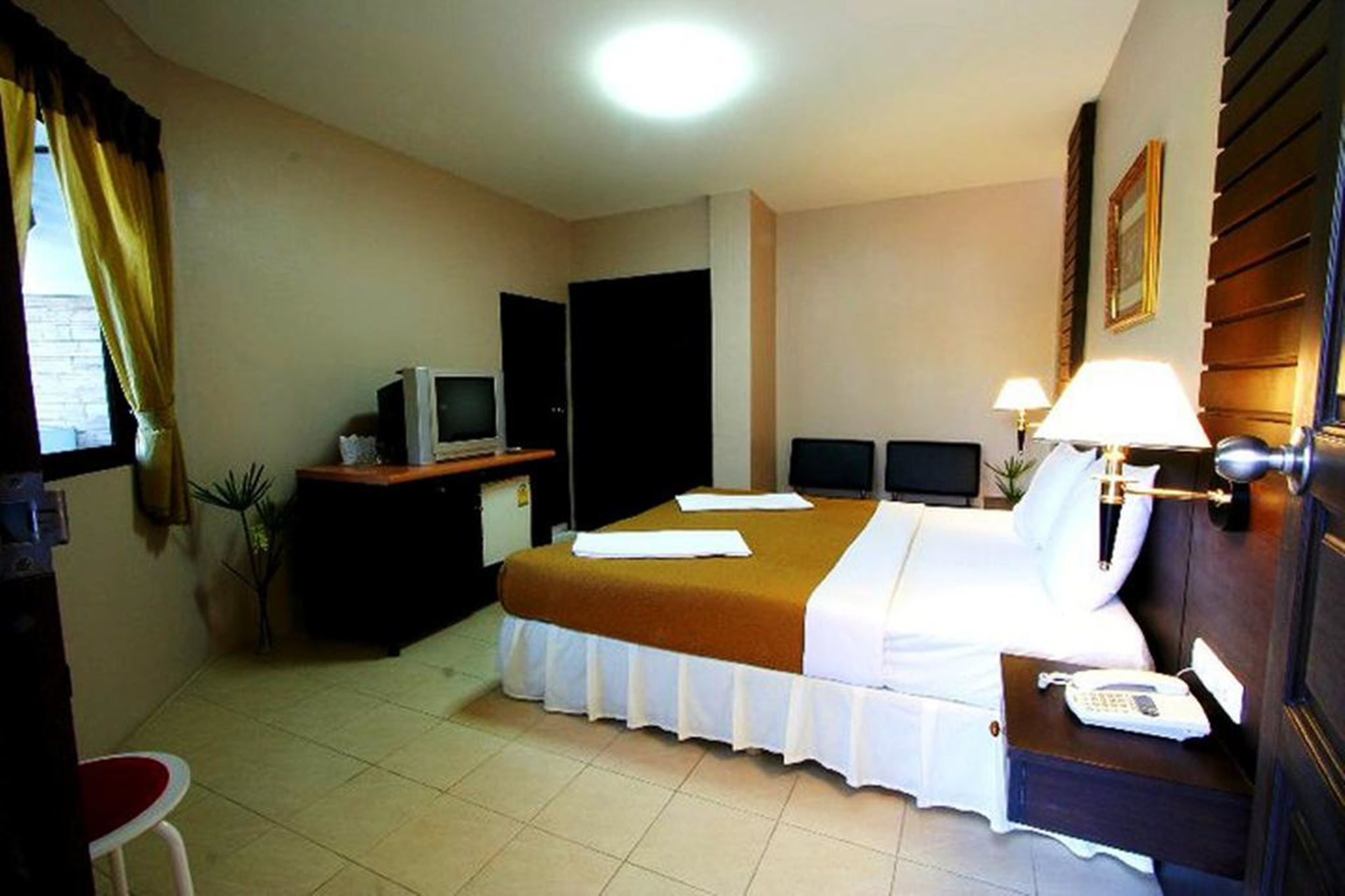 Een hotelkamer met een bed, nachtkastje, lamp, bureau met een computer en een stoel.