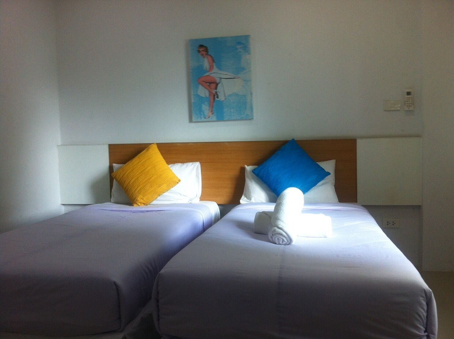 Een hotelkamer met twee bedden, elk met een ander kleurend kussen, een houten hoofdbord en een schilderij aan de muur.
