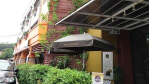 A building with a covered outdoor seating area, a sign indicating a reception area, and a banner with a logo. - PK Mansion (Wichit)