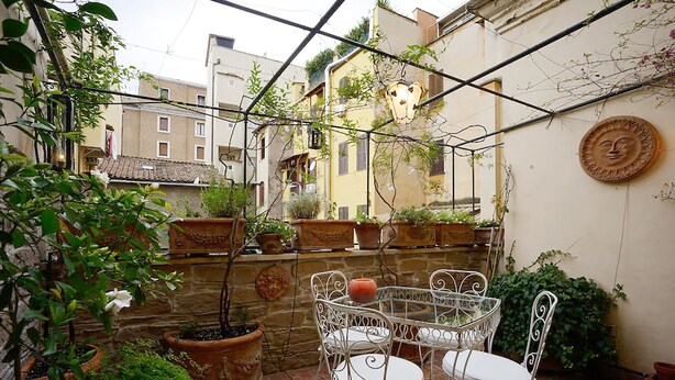 An outdoor patio with a metal table and chairs, surrounded by potted plants and a stone wall. - Vatican luxury home Terrazzo, 2 bedrooms 2 bathrooms a 50 yds from  S.Pietro (Roma)