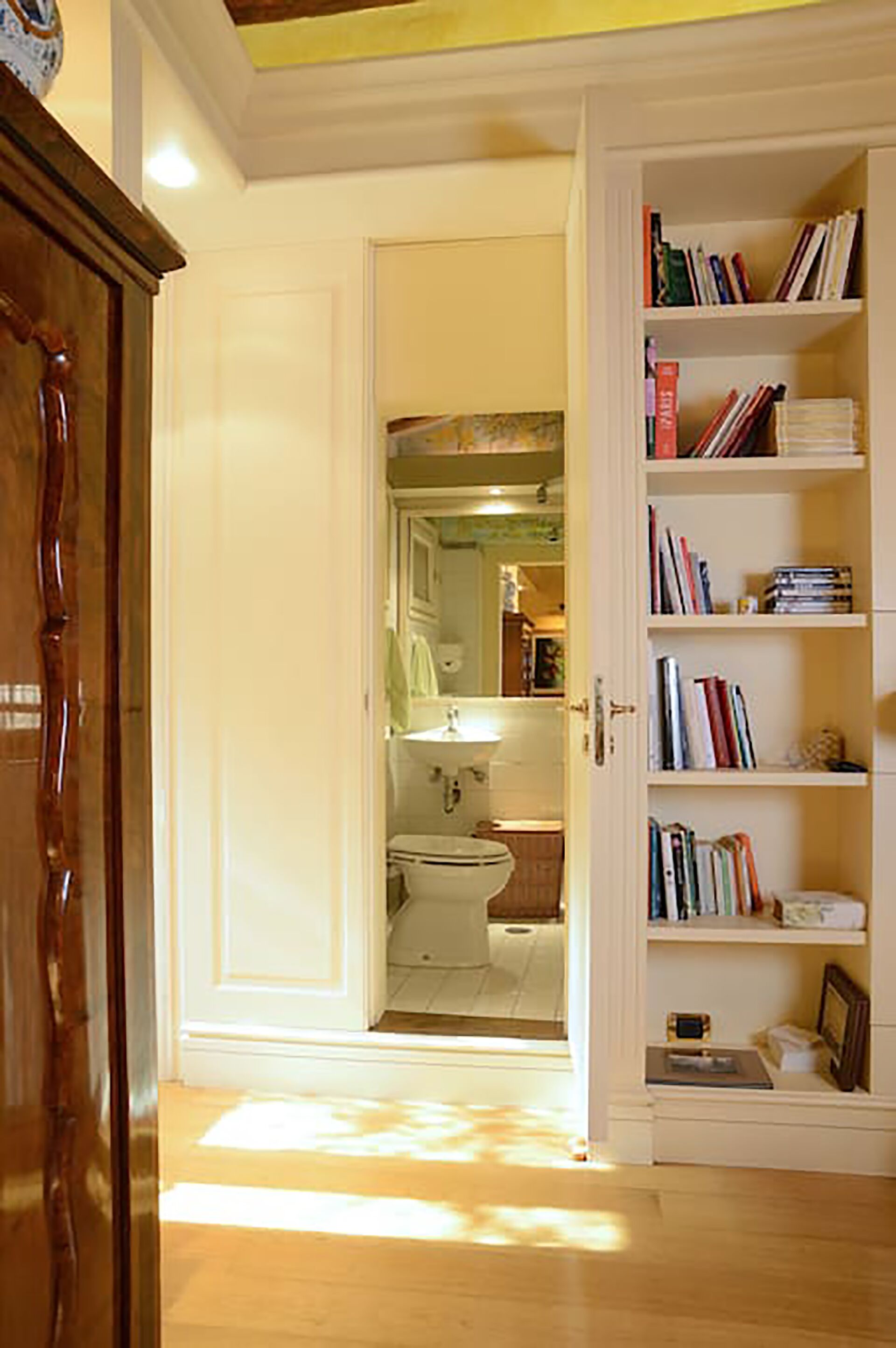 A hallway leading to a bathroom with a toilet and sink, and a bookshelf filled with books.