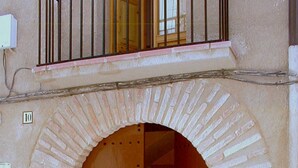 A building entrance with a large wooden door, an arched brick archway, and a metal railing above. - Spacious, original, cozy, flooded with light, fiberglass, autonomous (Torroja del Priorat)