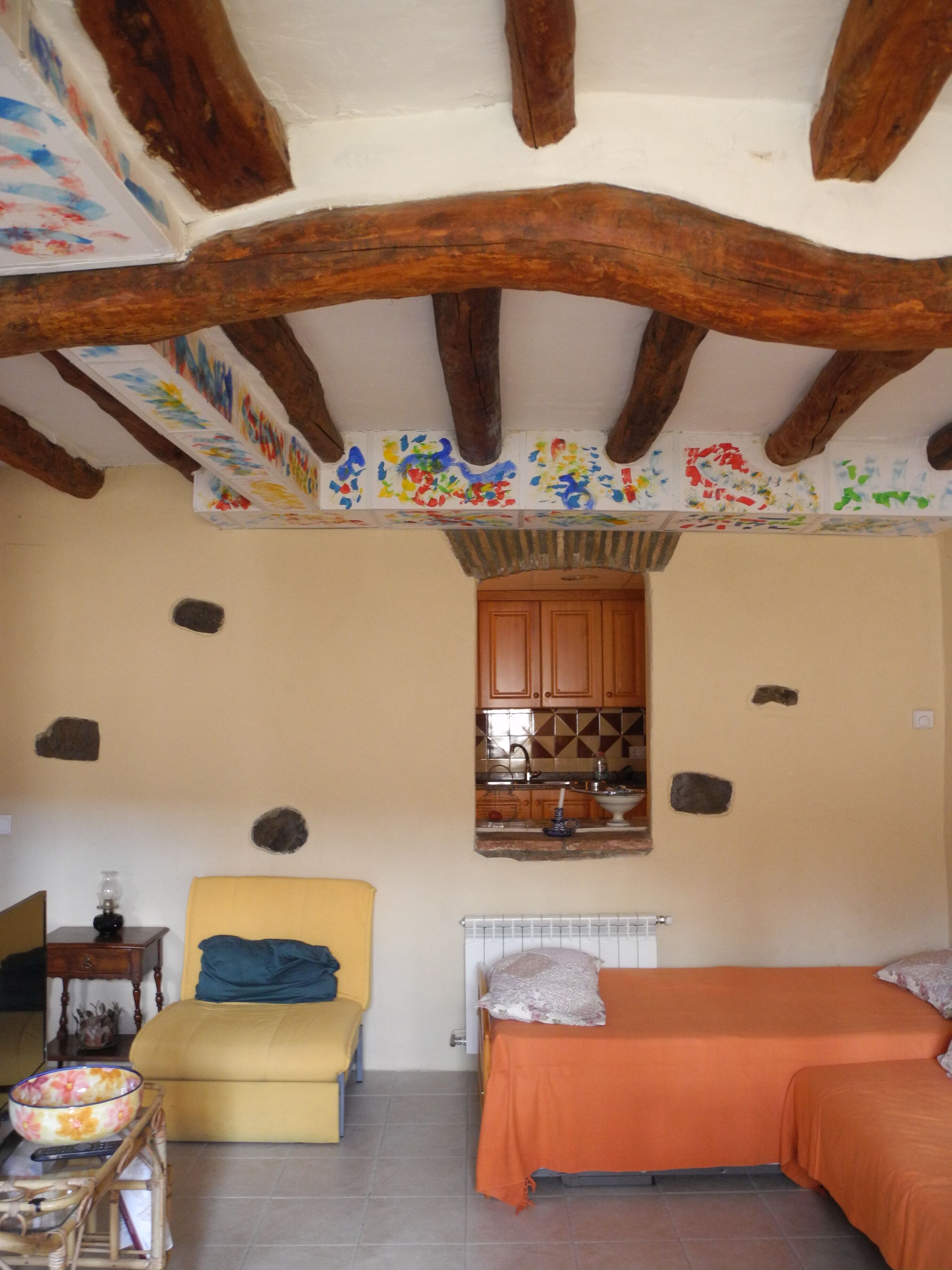 Una habitación con cama, sofá, una mesita con un cuenco y una zona de cocina con armarios y un radiador.