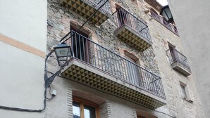 A building with a stone facade, multiple balconies with metal railings, and a large wooden door. - Spacious, original, cozy, flooded with light, fiberglass, autonomous (Torroja del Priorat)