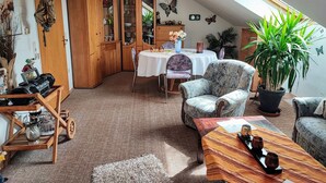 Una stanza accogliente con un tavolo da pranzo, sedie, un divano, una pianta in vaso e un mobiletto in legno.