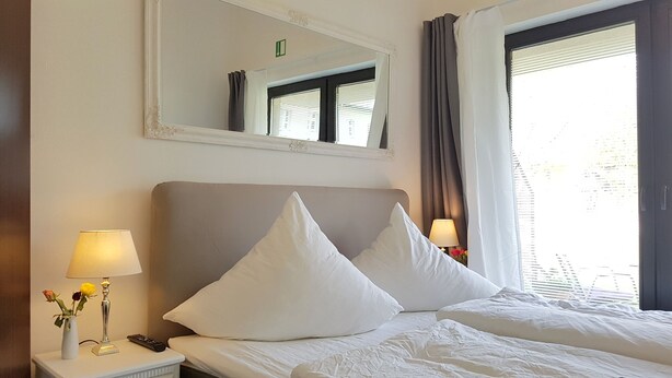 Hotellihuone, jossa on suuri sänky, yöpöytä lampun kanssa, peili ja ikkuna, jossa on verhot.