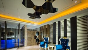 A modern lobby with a reception desk, two blue upholstered chairs, a small round table, and a unique geometric ceiling design. - Wei Feng Motel (Kaohsiung)