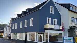 Ein zweistöckiges Hotel Gebäude mit dunkler Fassade, einem Balkon mit Metallgeländer und einem Schild, das eine Geschwindigkeitsbegrenzung von 30 km/h anzeigt.