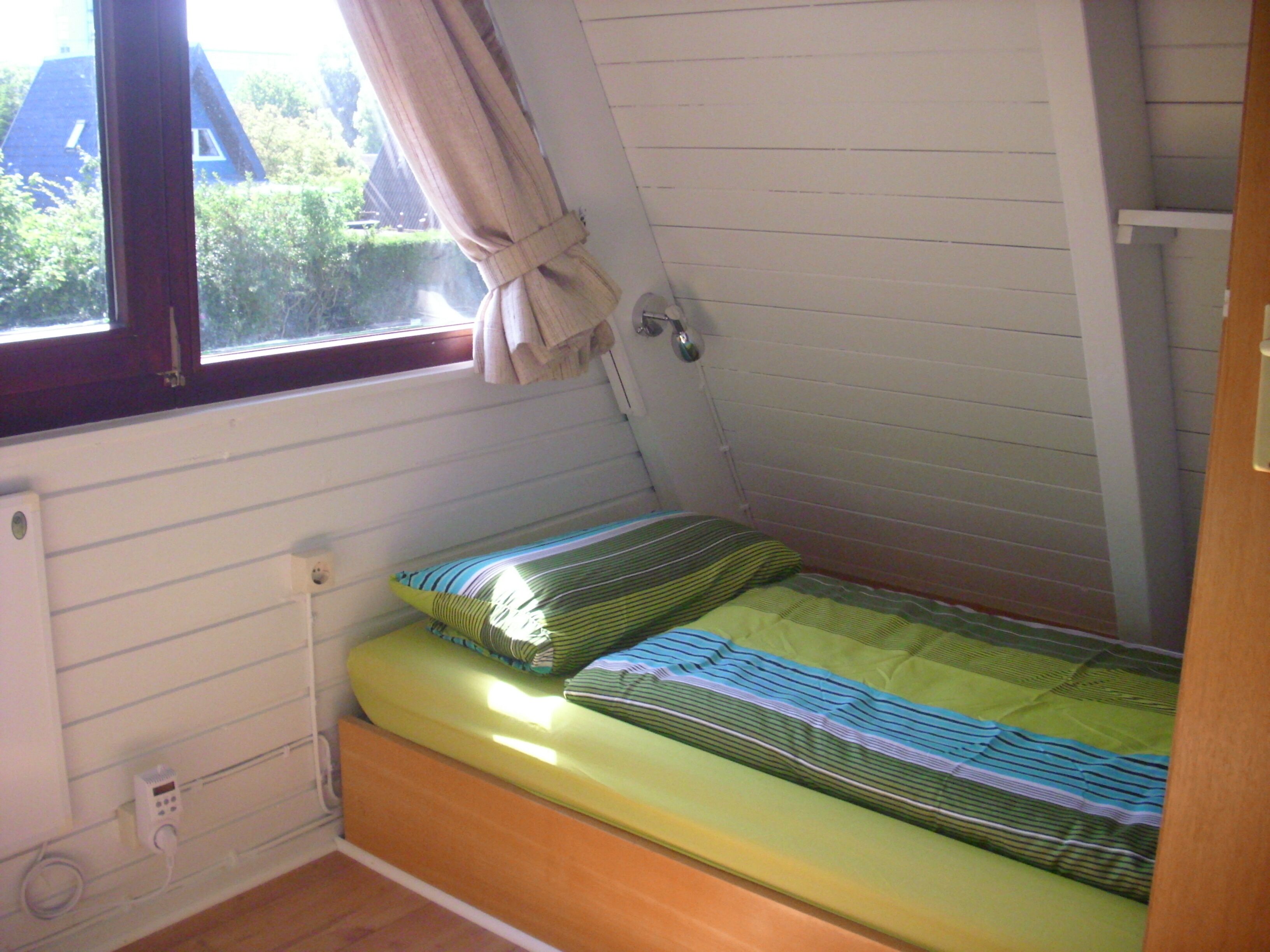 A small, single-bed room with a window, a radiator, and a power outlet.