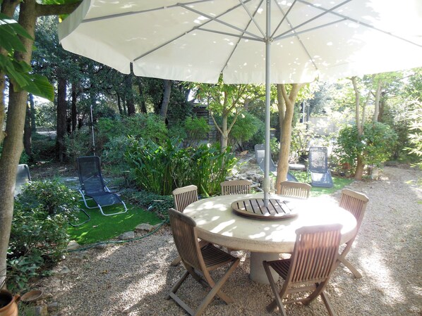 Una mesa redonda con seis sillas, un paraguas y un jardín con árboles y plantas.