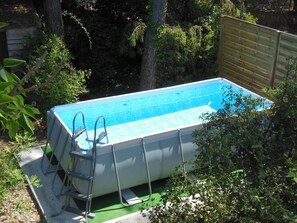Una piscina elevada con escalera, rodeada de árboles y una valla de madera.