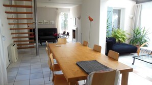 Ein geräumiger Essbereich mit einem langen Holztisch und Stühlen, einer schwarzen Couch und einer Treppe, die zu einer oberen Ebene führt.