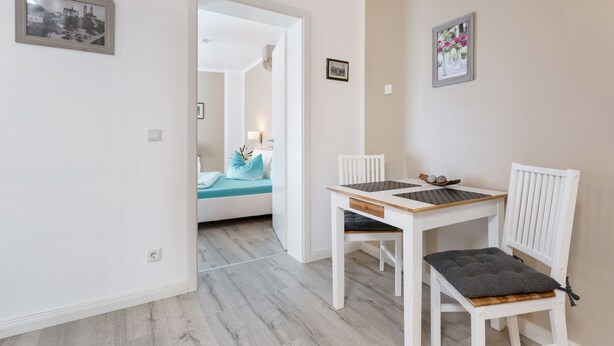 A room with a wooden dining table and chairs, a sofa with a teal cushion, and a small table with decorative items. - Small holiday home in beautiful Dresden  (Dresden)