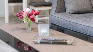A living room with a grey sofa, a small table with a vase of flowers, a remote control, and a lamp. - Small holiday home in beautiful Dresden  (Dresden)