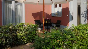 A patio with a table and chairs under a white umbrella, surrounded by greenery. - Small holiday home in beautiful Dresden  (Dresden)