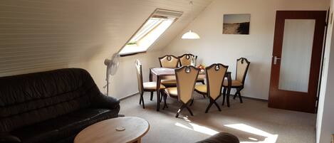 A cozy room with a sloped ceiling, a wooden ceiling, a dining table with chairs, a sofa, and a small round table.