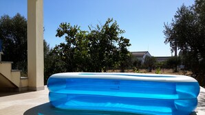 A clear blue inflatable pool in an outdoor setting with a tiled floor and trees in the background.