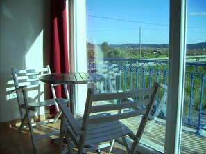 A balcony with a table and two chairs, a red curtain, and a view of a road and greenery.