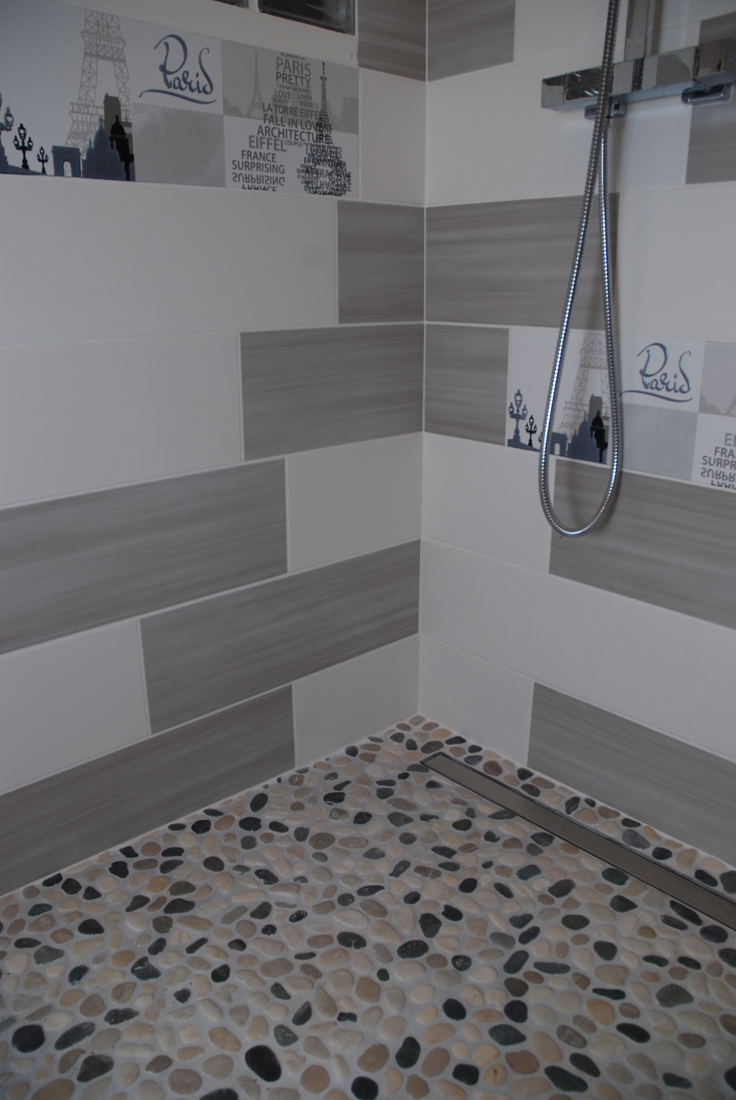 Une douche avec un sol à motifs de galets et un mur décoré sur le thème de Paris.