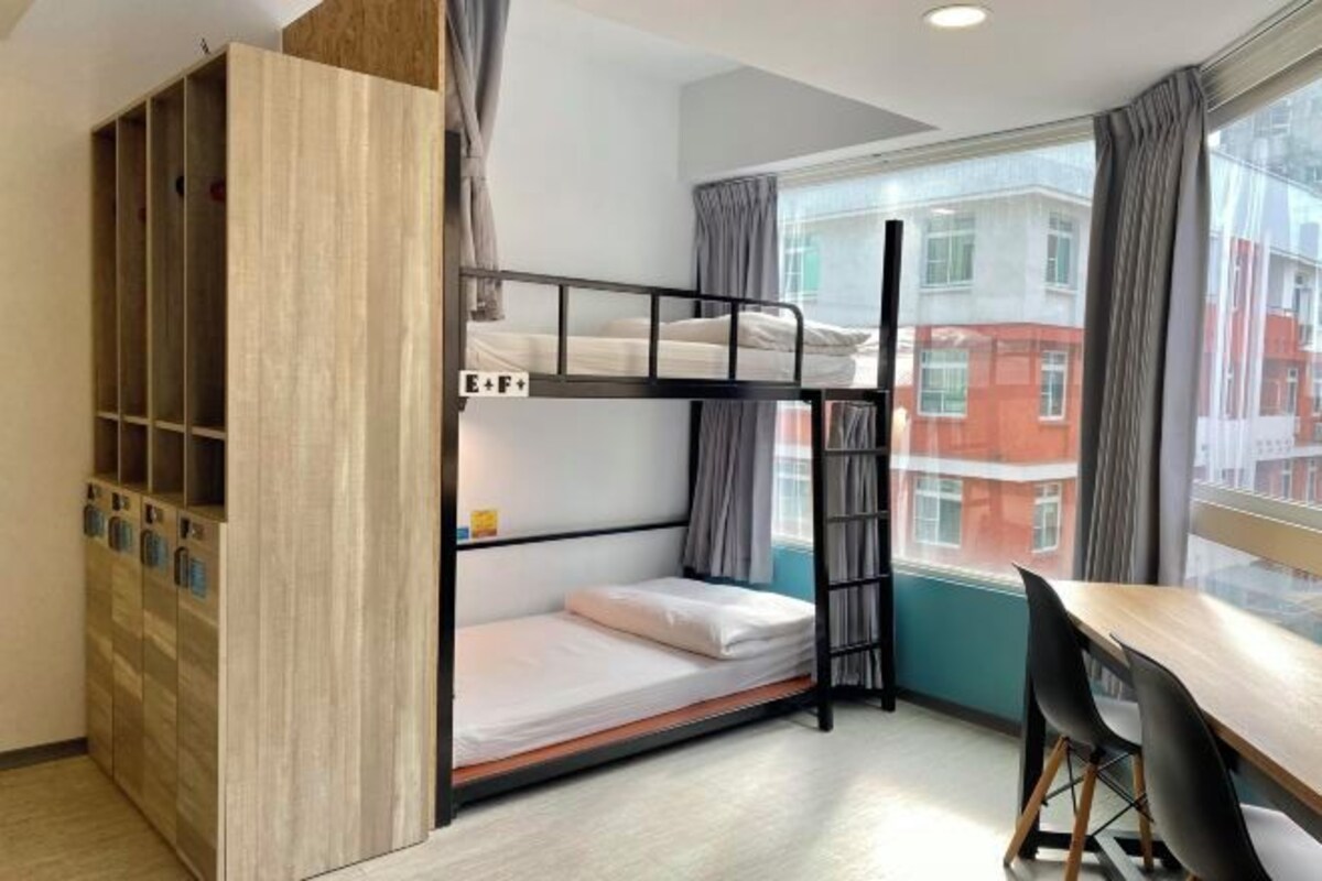 A bunk bed room with a desk and chair, a wardrobe, and a window with curtains.