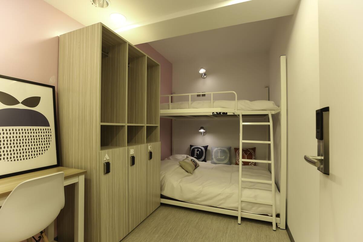 Ein Stockbett mit Schreibtisch und Kleiderschrank in einem Zimmer mit hellrosa Wänden.