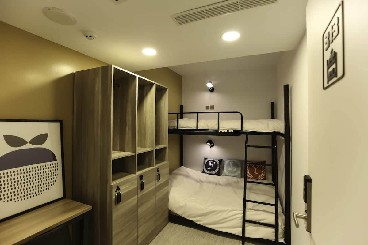 Ein Stockbett mit einer Leiter, ein Kleiderschrank mit vielen Fächern und ein kleiner Schreibtisch mit einem gerahmten Bild.