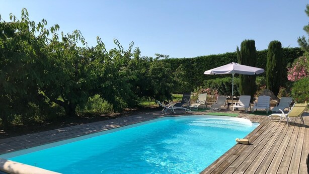 Une piscine dotée d’une terrasse en bois, entourée de verdure et de chaises longues.