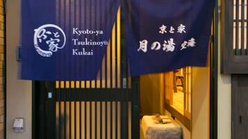 A traditional Japanese entrance with a black gate, a blue banner with white text, and a small stone lantern inside.