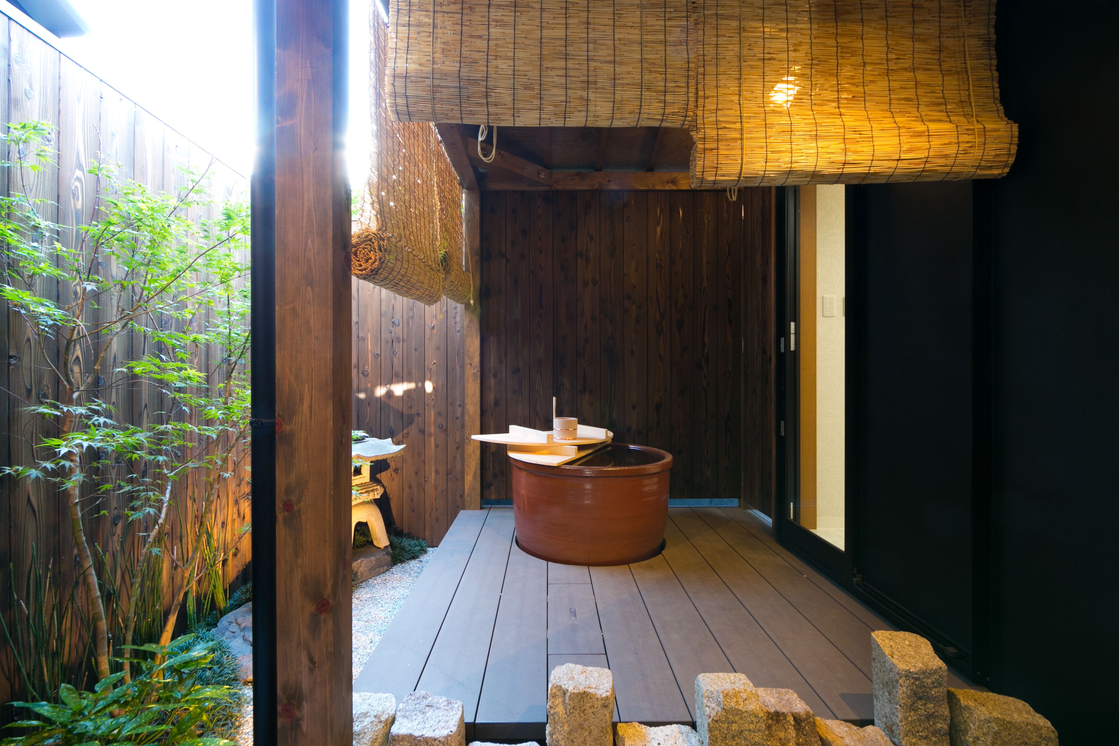 A traditional wooden bathhouse with a large clay tub, a small table, and a bamboo ceiling.