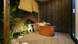 A wooden deck with a hot tub, a stone lantern, and a bamboo screen.