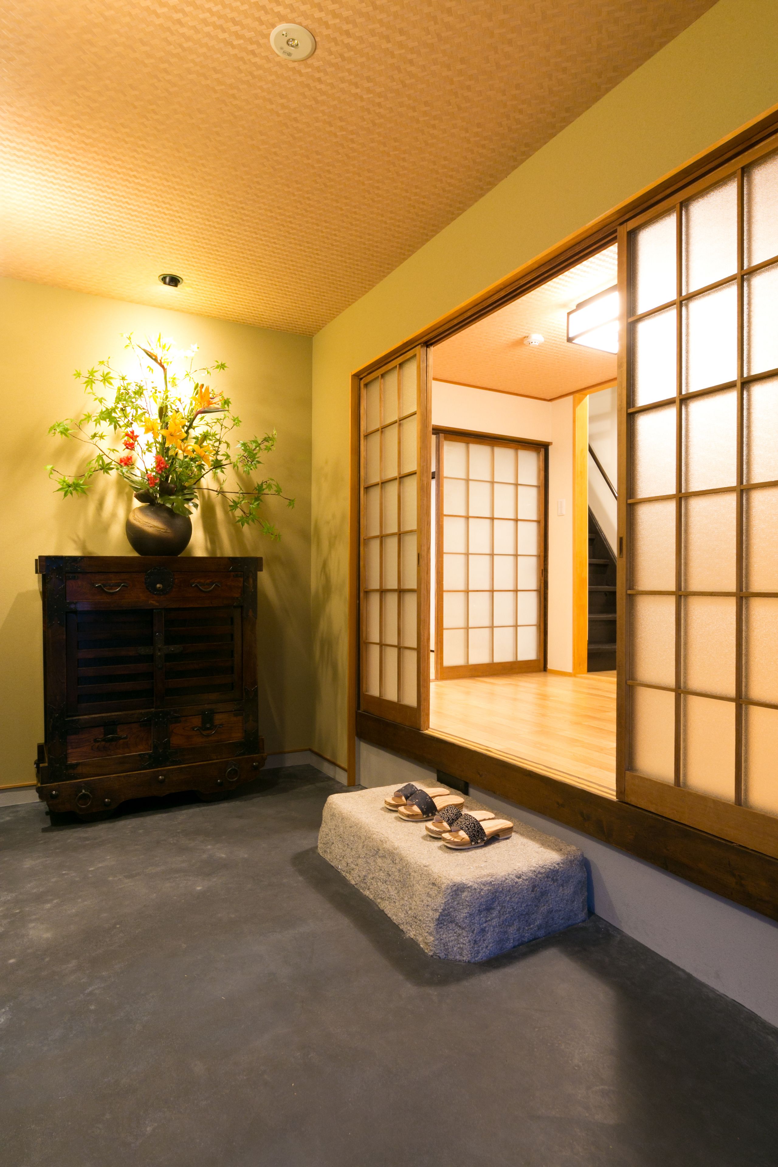 A traditional Japanese room with tatami flooring, a wooden cabinet with drawers, a vase with flowers, and a sliding shoji screen door.